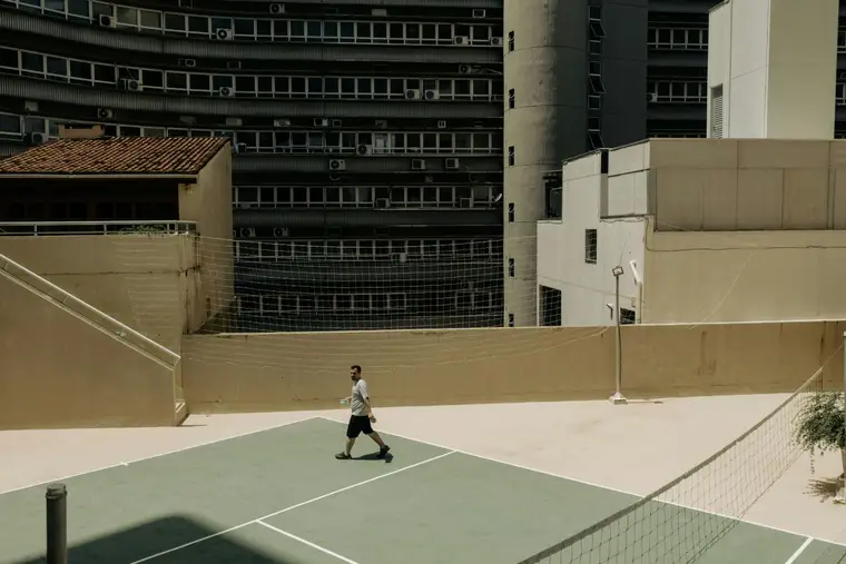 A lone figure crossing an empty court below a large apartment block