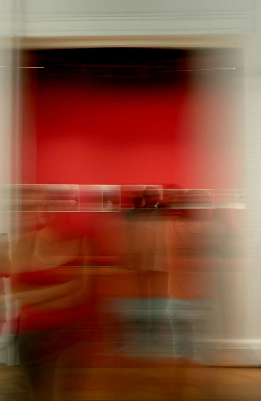 A room of people in motion, caught in a long exposure against a red wall