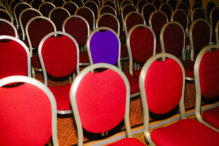 A single violet chair in rows of red banquet chairs