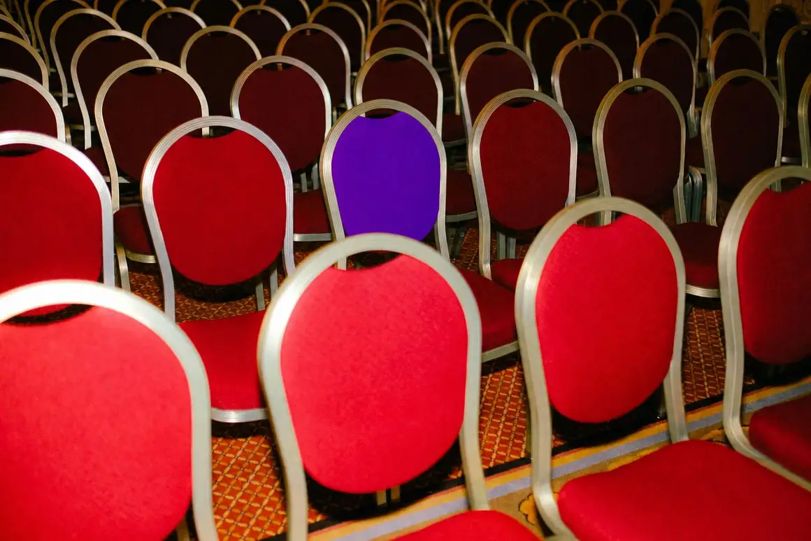 A single violet chair in rows of red banquet chairs