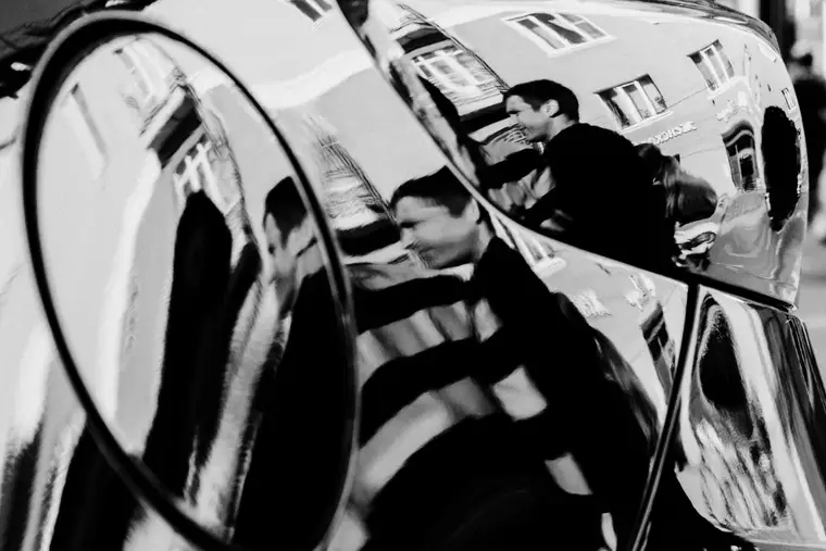 Two men reflected in the polished bodywork of a car on a street