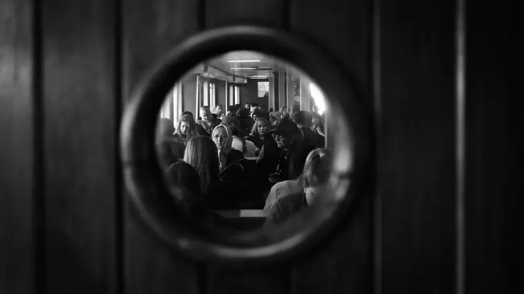 A crowded ferry cabin seen through a porthole in a wooden door
