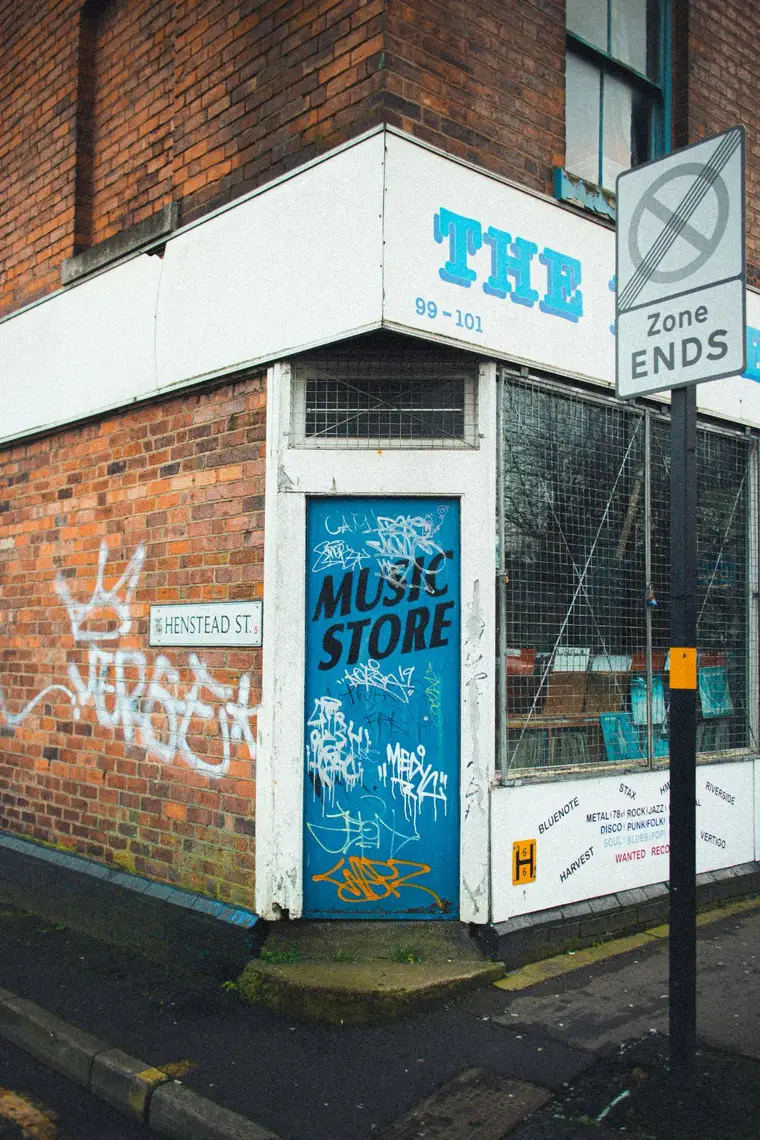 A graffiti covered corner music shop on a wet street